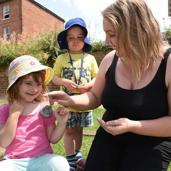A practitioner showing two children a snail in the garden