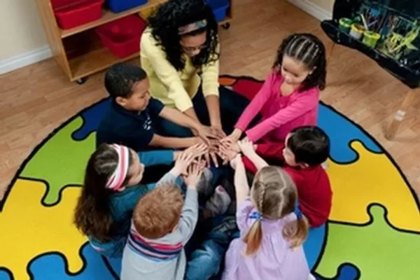 Children and a practitioner joining hands in a circle on a puzzle mat at Into-Play The Quays