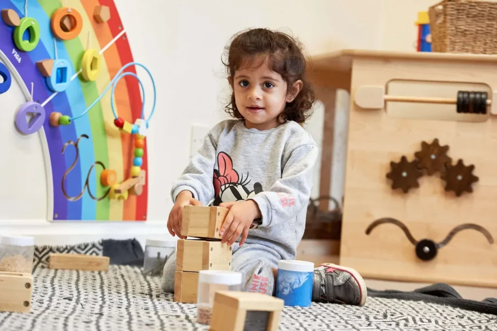 A young child sitting on a rug, stacking wooden blocks